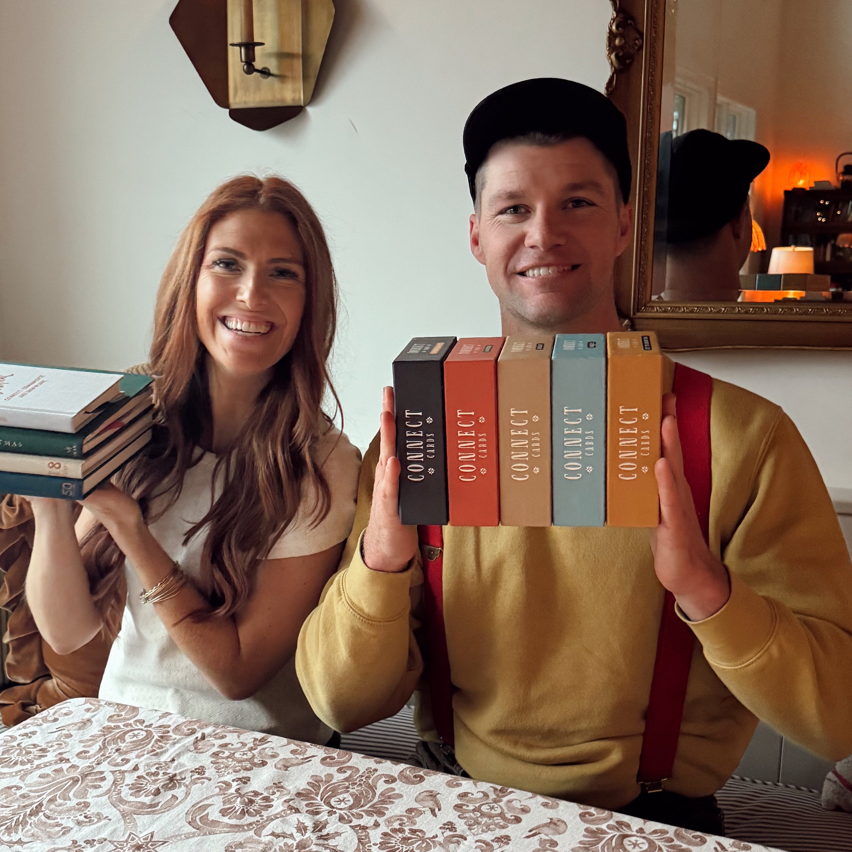 Two people holding books in a cozy room with a mirror and window.